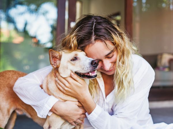 Woman with wavy hair embraces a smiling tan dog.